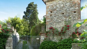 A stone building with a rustic appearance, surrounded by lush greenery and red flowers. - Rustic House in Tuscany With Shared Pool (San Giuliano Terme)