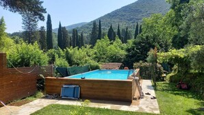 A swimming pool with a wooden deck, surrounded by a lush garden and a hilly backdrop. - Rustic House in Tuscany With Shared Pool (San Giuliano Terme)