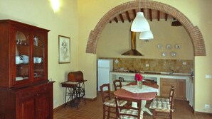 A dining area with a table, chairs, a cabinet, and a kitchen in the background. - Rustic House in Tuscany With Shared Pool (San Giuliano Terme)
