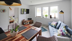 A modern living room with a wooden dining table, a sofa, and a TV mounted on the wall. - Cottage, Oldenswort (Oldenswort)