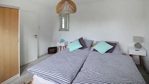 A bedroom with a bed, bedside tables, a hanging light fixture, and a door. - Cottage, Oldenswort (Oldenswort)