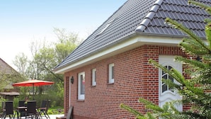 A brick house with a tiled roof, a patio with a table and chairs, and a red umbrella. - Cottage, Oldenswort (Oldenswort)