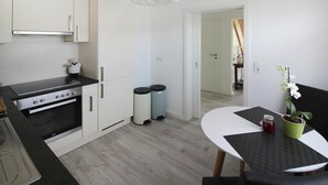 A modern kitchen with white cabinets, a black countertop, and a built-in oven. There is a dining area with a table and chairs, and a potted orchid on the table. - Cottage, Oldenswort (Oldenswort)