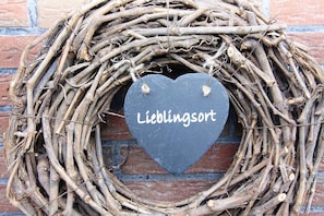 A heart-shaped sign with the text "Lieblingsort" attached to a woven wreath against a brick wall. - Reihenhaus Land and Sea, Buesum (Westerdeichstrich)
