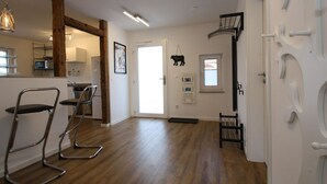 Une cuisine moderne avec des poutres en bois, un coin repas avec des chaises en métal et une porte blanche ornée d’une décoration représentant une vache noire.