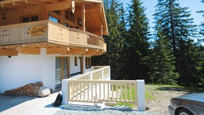 A wooden chalet with a balcony, a stone wall, and a car parked nearby. - Chalet in Konigsleiten With Wellness & Alps View (Krimml)