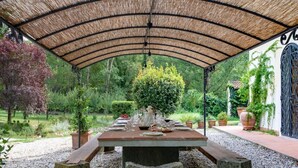 An outdoor dining area with a covered table set for a meal, surrounded by greenery and a garden. - Villa Privata "Forre 563 " (Reggello)