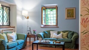 A living room with two green sofas, a coffee table, a window with a view of greenery, and a wall-mounted picture frame. - Villa Privata "Forre 563 " (Reggello)