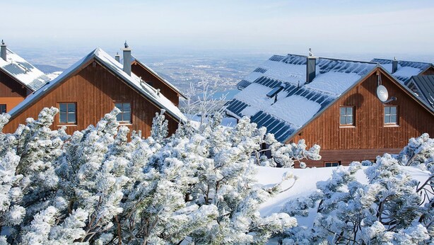 Een houten blokhut met een schuin dak, zonnepanelen en sneeuwbedekte bomen.