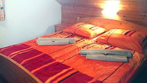 Een bed met een rood-oranje gestreepte spreidekker, twee kussens en twee opgevouwen handdoeken.