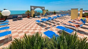Une terrasse sur le toit, avec des fauteuils bleus, un sol à carreaux et une vue sur la mer.