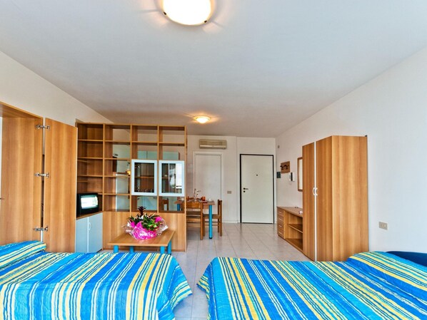 Une chambre avec deux lits, un bureau avec une chaise, une télévision et une armoire.
