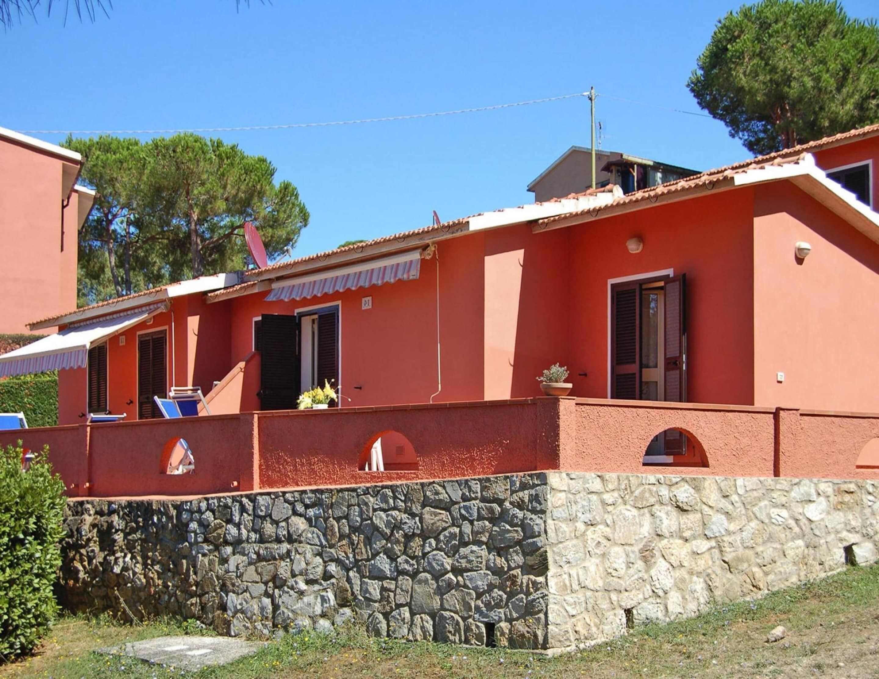 Un edificio rojo con base de piedra, un balcón con sillas de tomar el sol y una pequeña ventana con una planta en maceta.