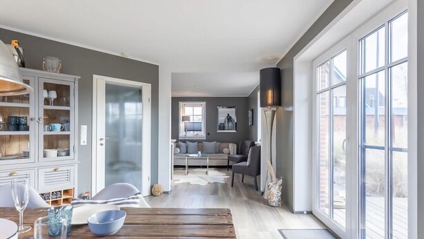 A modern living room with a sofa, a coffee table, and a dining area with a wooden table and chairs. - Wundervolles Ferienhaus fur Tating (Tating)
