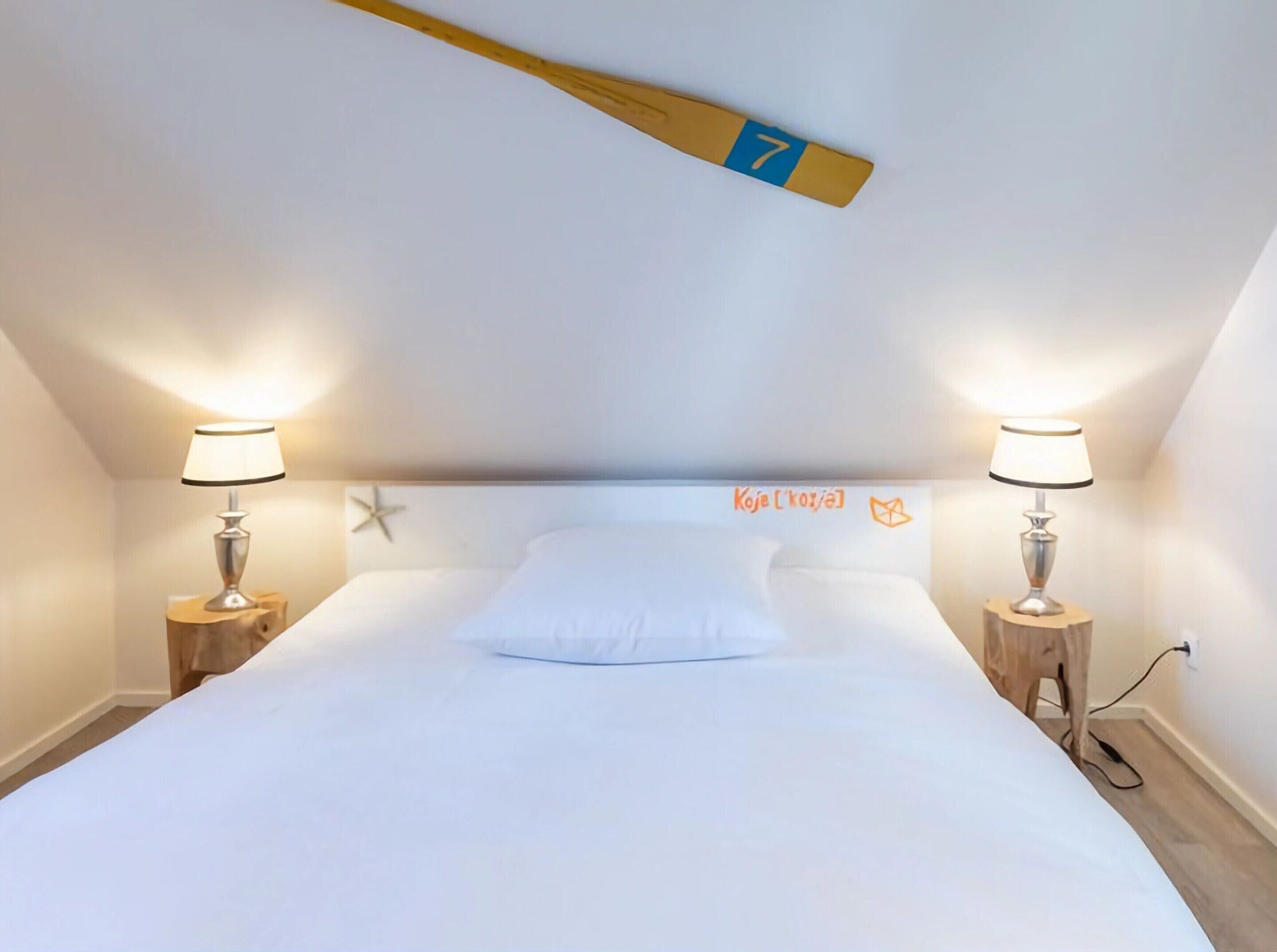 Una camera da letto con un letto bianco, due lampade ai lati del letto, una decorazione a stella sulla testiera e un pipistrello appeso al soffitto.