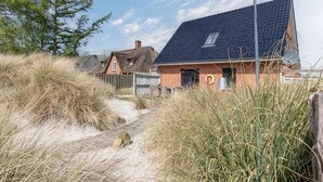 A coastal house with a sloped roof, a visible chimney, and a pathway leading to the entrance. - Wundervolles Ferienhaus fur Tating (Tating)