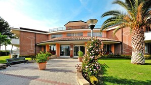 A building with a curved facade, a central entrance, and a surrounding garden with potted plants and a palm tree. - Villa in Cecina Mare Near Sandy Beaches (Cecina)