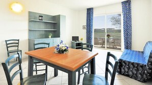 A dining area with a wooden table and chairs, a blue sofa, a TV, and a balcony with a view of the outdoors. - Villa in Cecina Mare Near Sandy Beaches (Cecina)