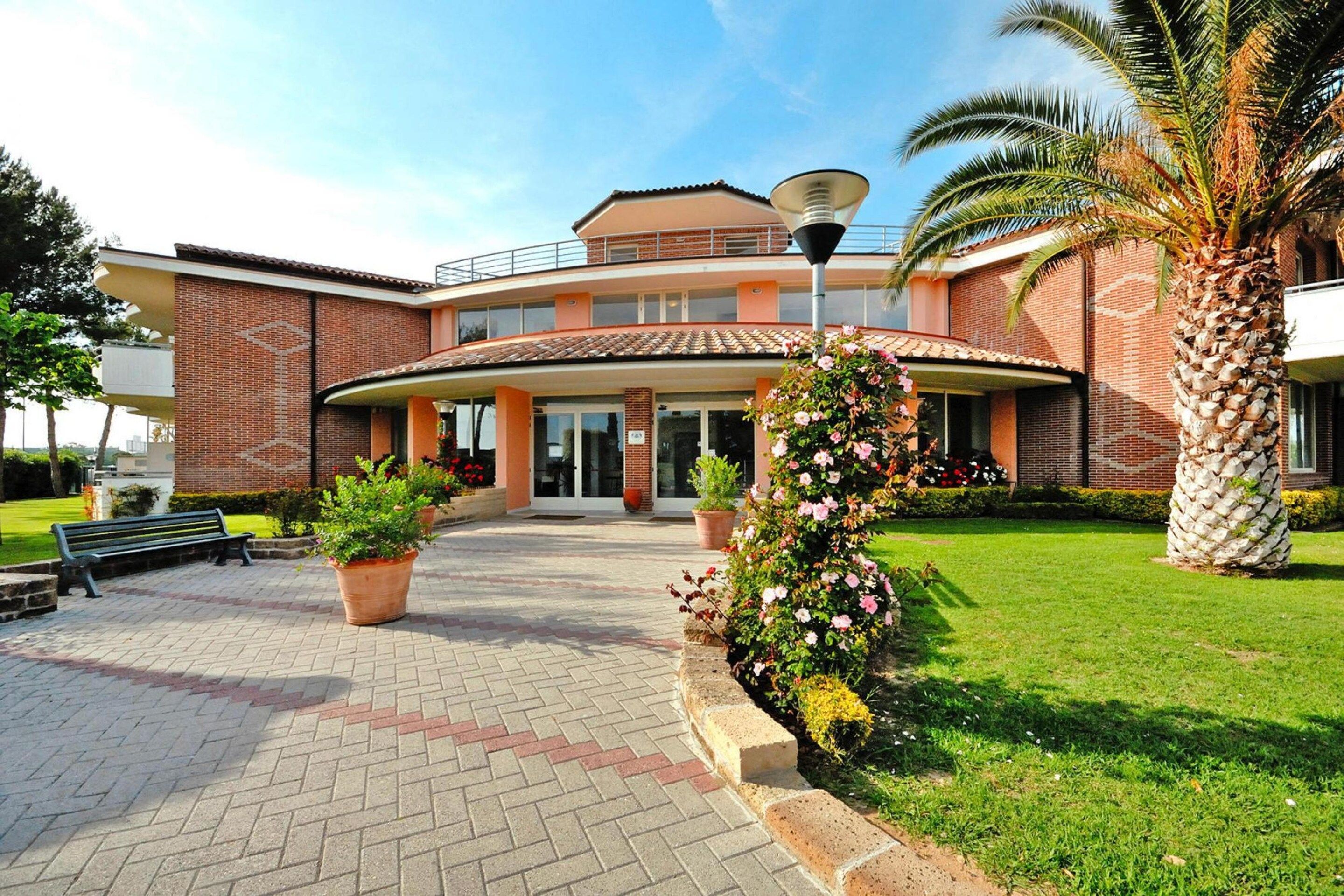 A two-story building with a curved entrance, a paved walkway, and potted plants.