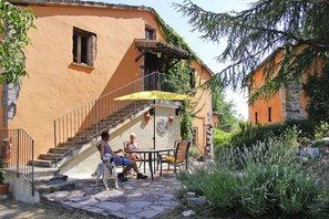 A stone staircase leading to a balcony with a yellow umbrella, a dog, and two people sitting at a table. - Villa Ca" Piero, Urbino (Urbino)