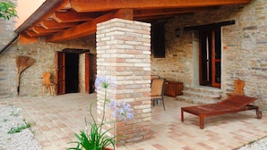 Un edificio de piedra con una pérgola de madera, un pilar de ladrillo y una silla de lounge de madera.