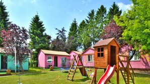 Un terrain de jeux avec un toboggan et des balançoires, entouré de maisons aux couleurs vives.