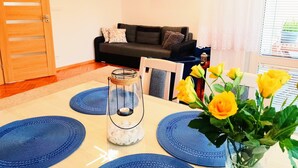 En stue med en trædør, en sofa, to billeder, en vase med gule blomster og et bord med blå servietringe og en lysestage.