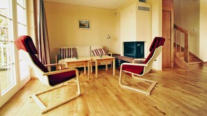 A living room with a wooden floor, a sofa, two rocking chairs, a TV, and a staircase. - Cottage Directly by the Lake in Trygor (Wegorzewo)