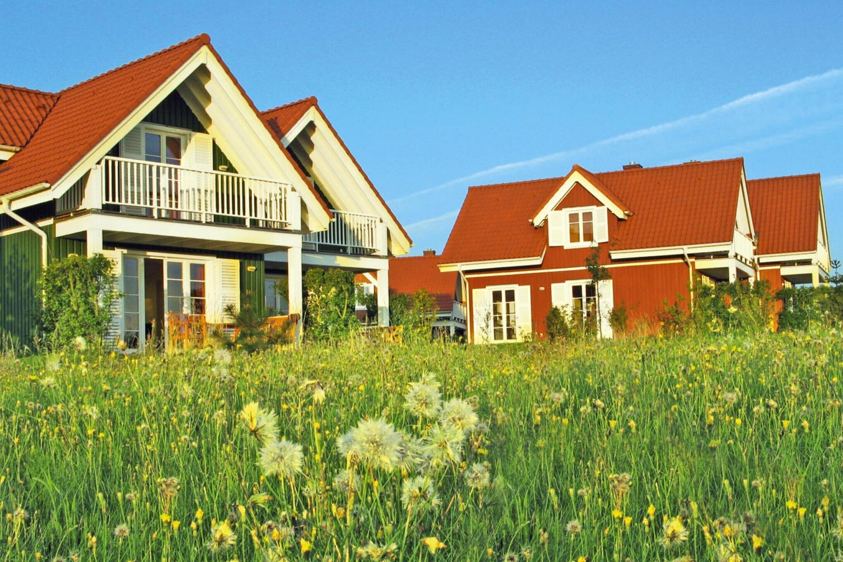 A row of houses with red roofs and white trim, surrounded by a field of tall grass and wildflowers.
