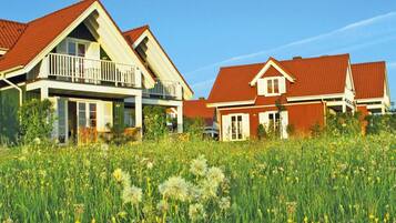 A row of houses with red roofs and white trim, surrounded by a field of tall grass and wildflowers.