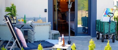 An outdoor patio with wicker furniture, a table with drinks, a green cart, and small trees.