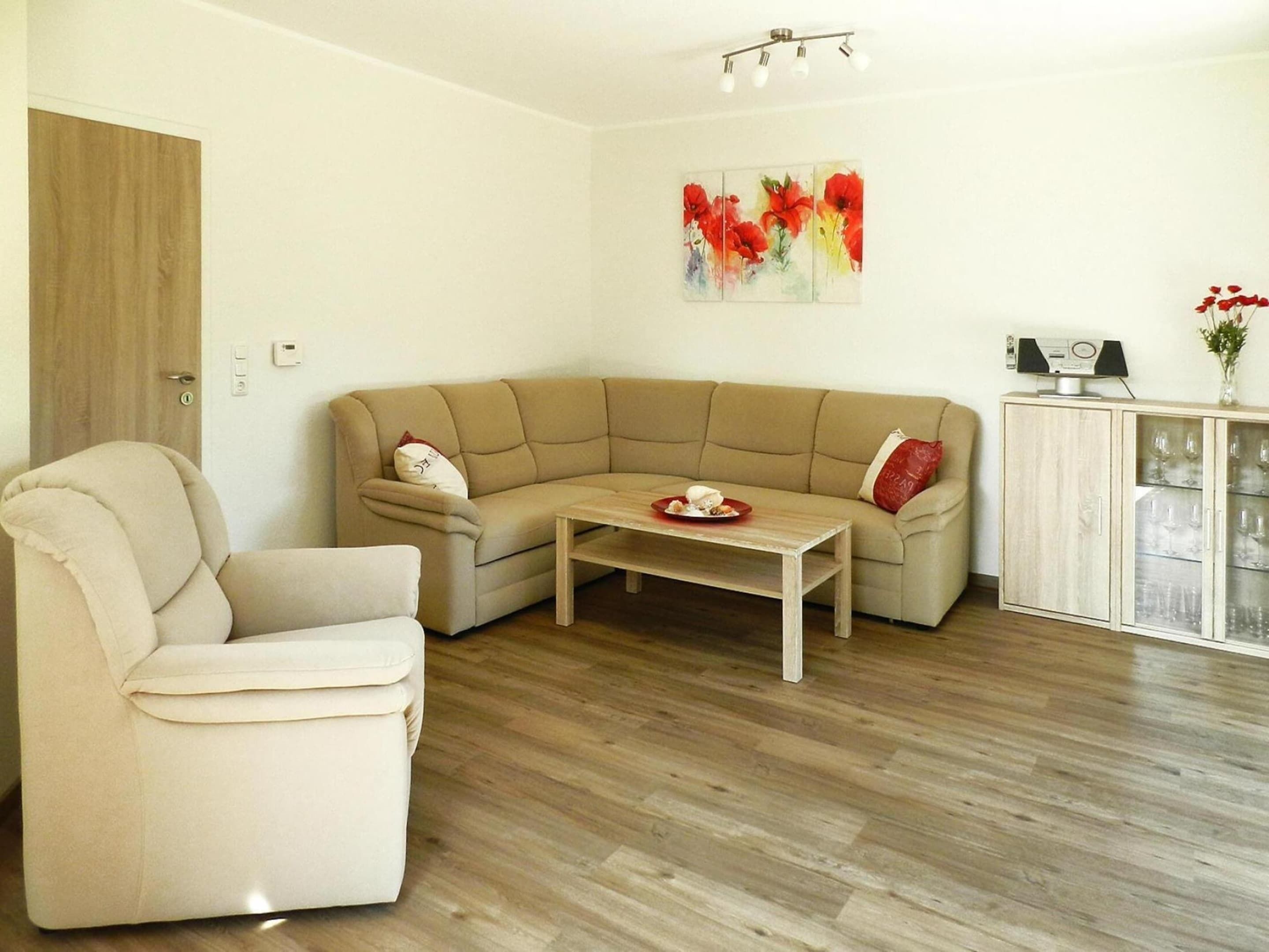 Un salon avec un canapé beige, une table basse en bois, un fauteuil blanc et un meuble avec des portes en verre.