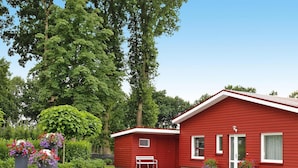A red single-story house with a white door, a small porch, and a well-maintained lawn. - Ferienwohnung Landblick, Rastede (Rastede)
