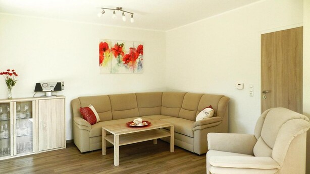 A living room with a beige sofa, a wooden coffee table, a white armchair, and a cabinet with glass doors. - Ferienwohnung Landblick, Rastede (Rastede)