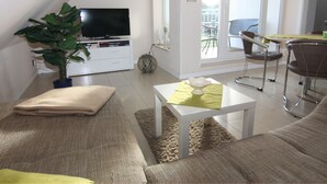 A modern living room with a flat-screen TV, a large plant, and a dining area with a table and chairs. - Appartementhaus Strandloper, Zinnowitz (Zinnowitz)