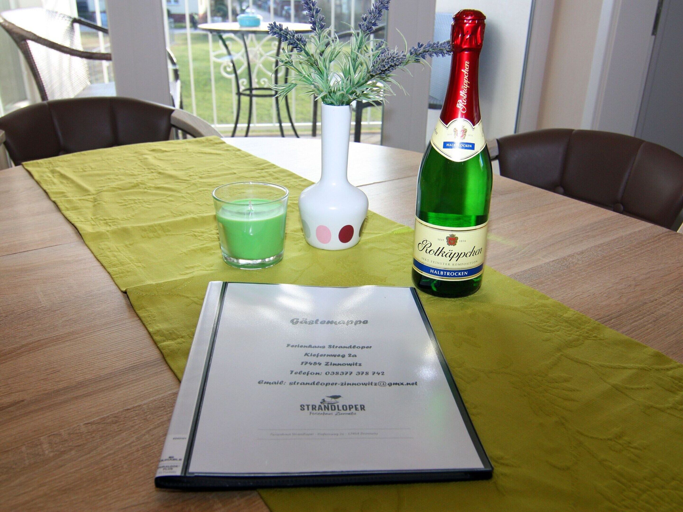 Ein Tisch mit grüner Tischdecke, eine Flasche Rotschkippchen, ein Glas grünes Getränk, eine weiße Vase mit Lavendel und eine Speisekarte.