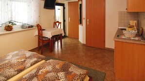 A cozy room with a wooden ceiling, a dining table with chairs, a TV mounted on the wall, and a kitchen area with a sink and countertop. - Reihenhaus in Lubben an der Spree (Lübben (Spreewald))