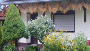 A house with a front porch, a neatly trimmed tree, and a flower bed with yellow and white flowers. - Reihenhaus in Lubben an der Spree (Lübben (Spreewald))