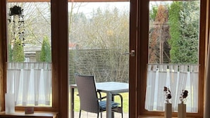 Ein Zimmer mit Holzvertäfelung, einem Tisch mit Stühlen und Blick durch eine Glastür auf einen Außenbereich mit Bäumen.