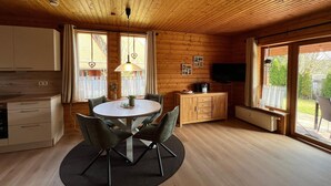 Ein Interieur einer Holzhütte mit Esstisch, Stühlen, einer Küchenzeile und einem Fernseher.