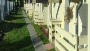 Eine Reihe identischer, eingeschossiger Blockhütten mit flachem Dach und kleiner Veranda, verbunden durch einen gepflasterten Weg.
