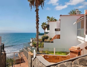 A coastal property with a view of the sea, featuring a stone staircase, a white building with a tiled roof, and a palm tree. - Holiday Flat With sea View in Maspalomas (San Bartolomé de Tirajana)