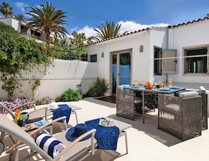 A patio with outdoor furniture, a table set with food and drinks, and a white building with a tiled roof. - Holiday Flat With sea View in Maspalomas (San Bartolomé de Tirajana)