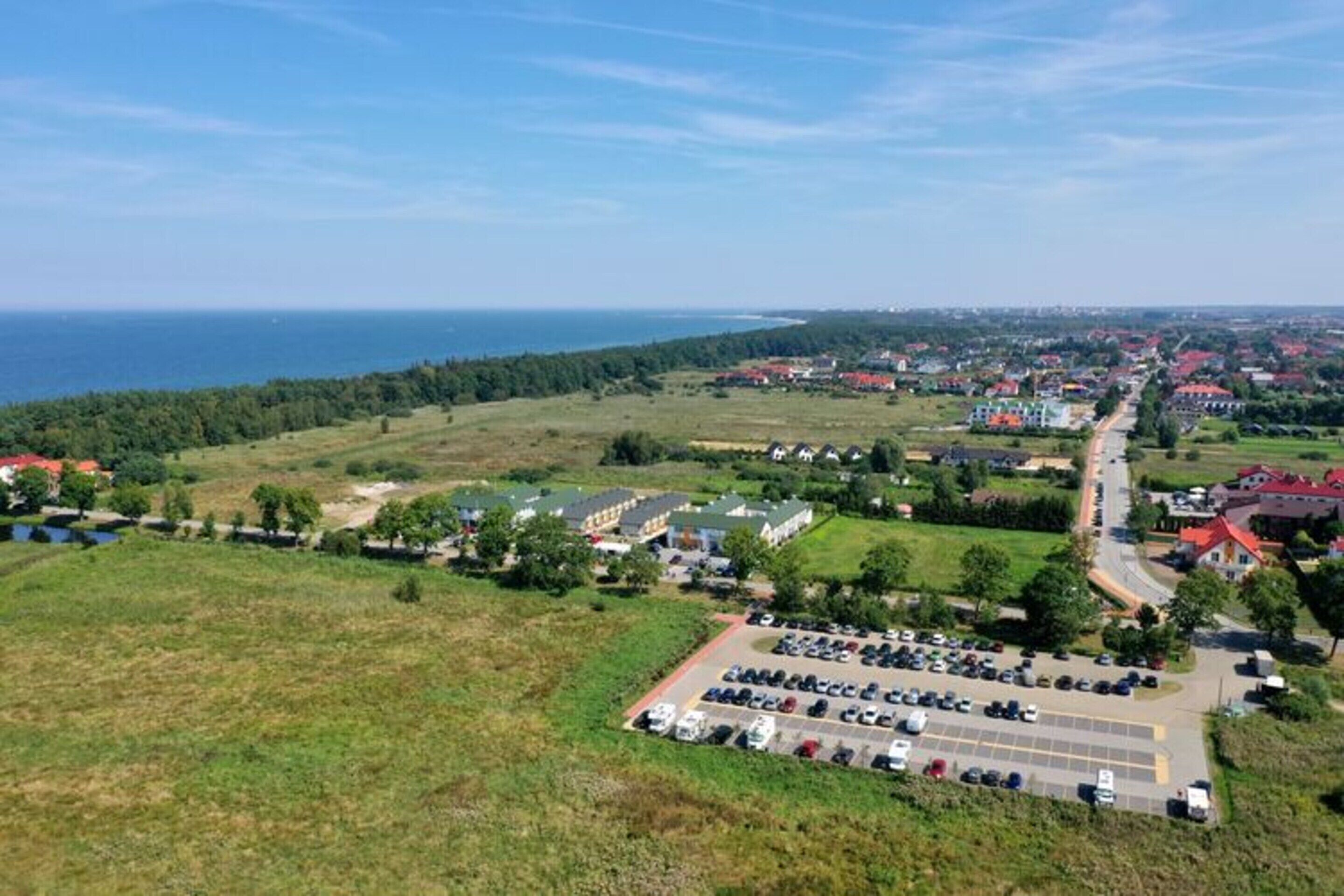 Eine Vogelperspektive einer Küstenstadt mit Parkplatz, Gebäuden und einer Straße, die zum Meer führt.
