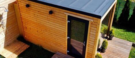 A small wooden cabin with a black roof, a sliding door, and a deck.