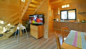 A wooden cabin interior with a TV, wooden dining table, chairs, a kitchen area, and a staircase. - Holiday Homes Close to the Beach, Pool, Sauna (Kołobrzeg)