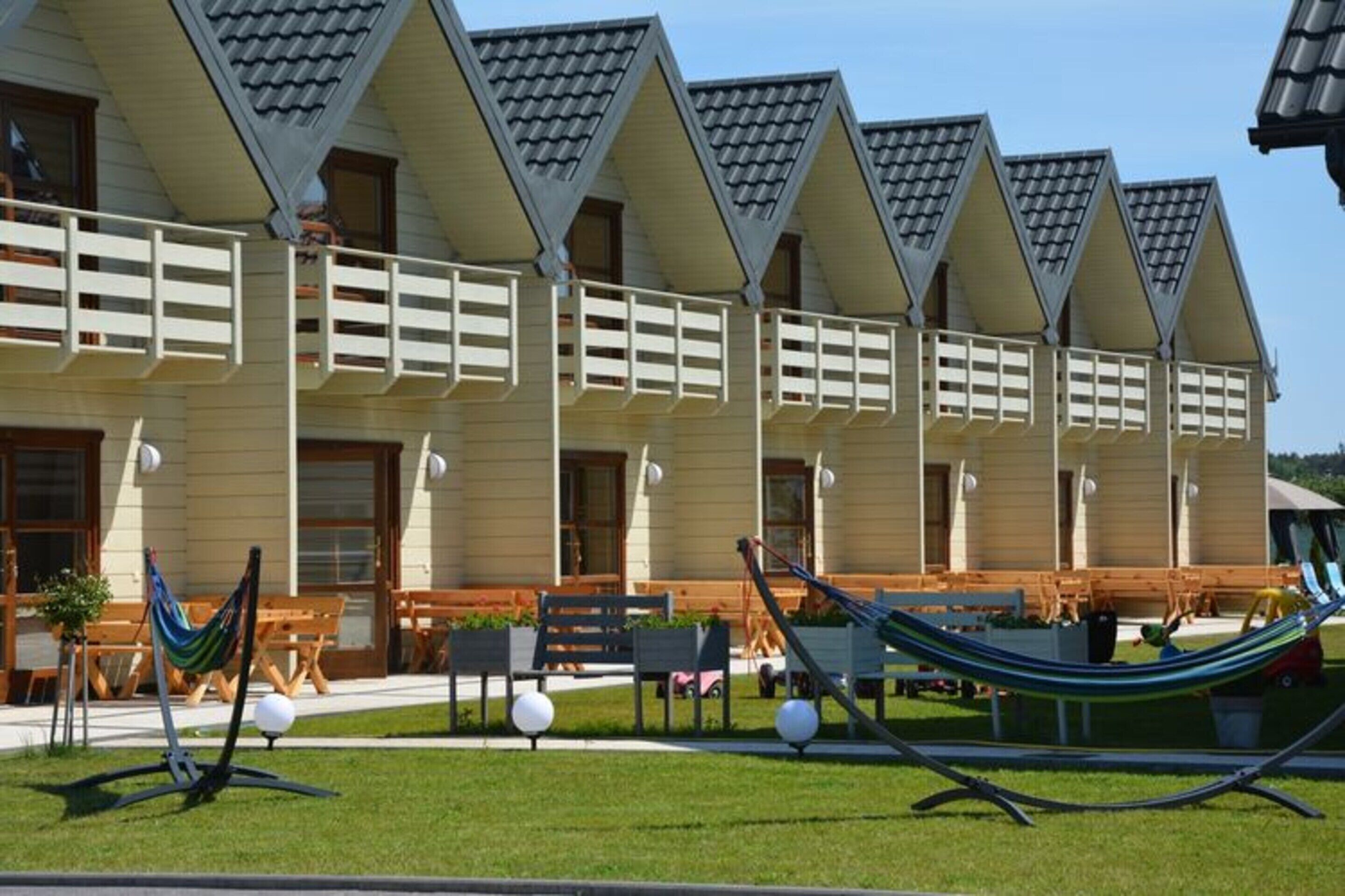 A row of beach houses with sloped roofs and balconies, a grassy lawn, and hammocks.