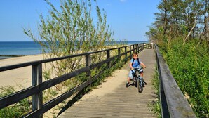 A wooden boardwalk leading to a beach with a person riding a bicycle. - Holiday Homes Close to the Beach, Pool, Sauna (Kołobrzeg)
