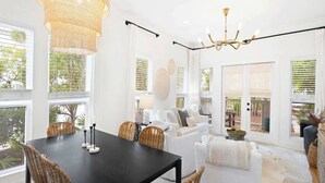 Amplia sala con diseño abierto, con una mesa de comedor, sillas de mimbre, un sofá blanco y una araña.