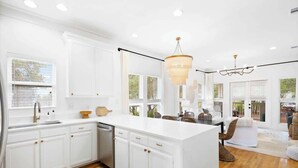 Una cocina moderna con armarios blancos, una isla grande y una zona de comedor con mobiliario de mimbre.